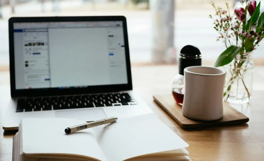 Laptop naast een opengeslagen boek op een bureau