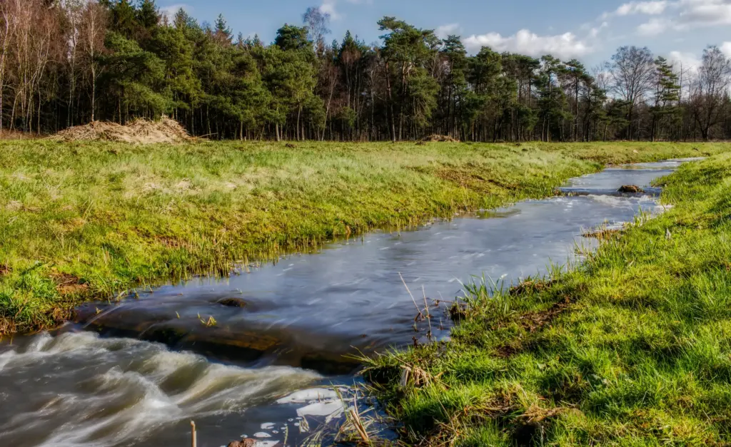 Beek door een groen weiland onder een blauwe lucht